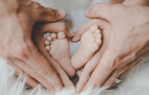 föräldrar som bildar ett hjärta med sina händer runt två babyfötter